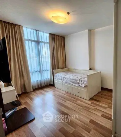 Cozy bedroom with wooden flooring and large window, featuring a daybed and elegant curtains.