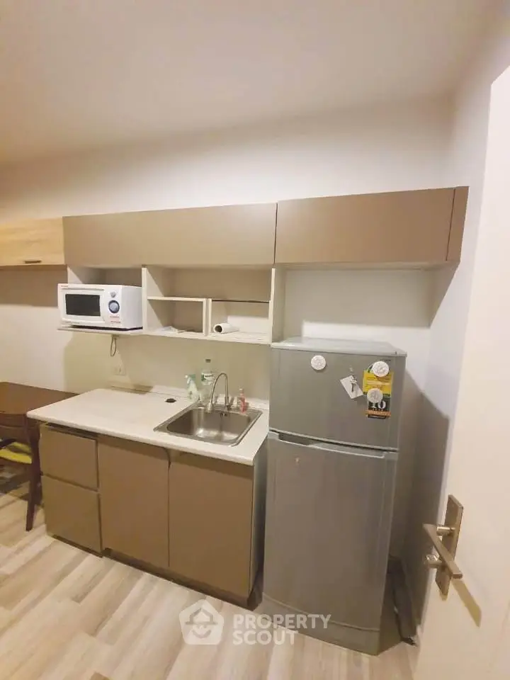 Modern compact kitchen with sleek cabinetry and stainless steel fridge in cozy apartment.
