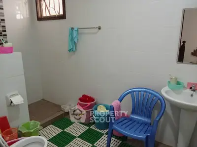 Spacious bathroom with colorful buckets and a plastic chair, tiled walls and floor.