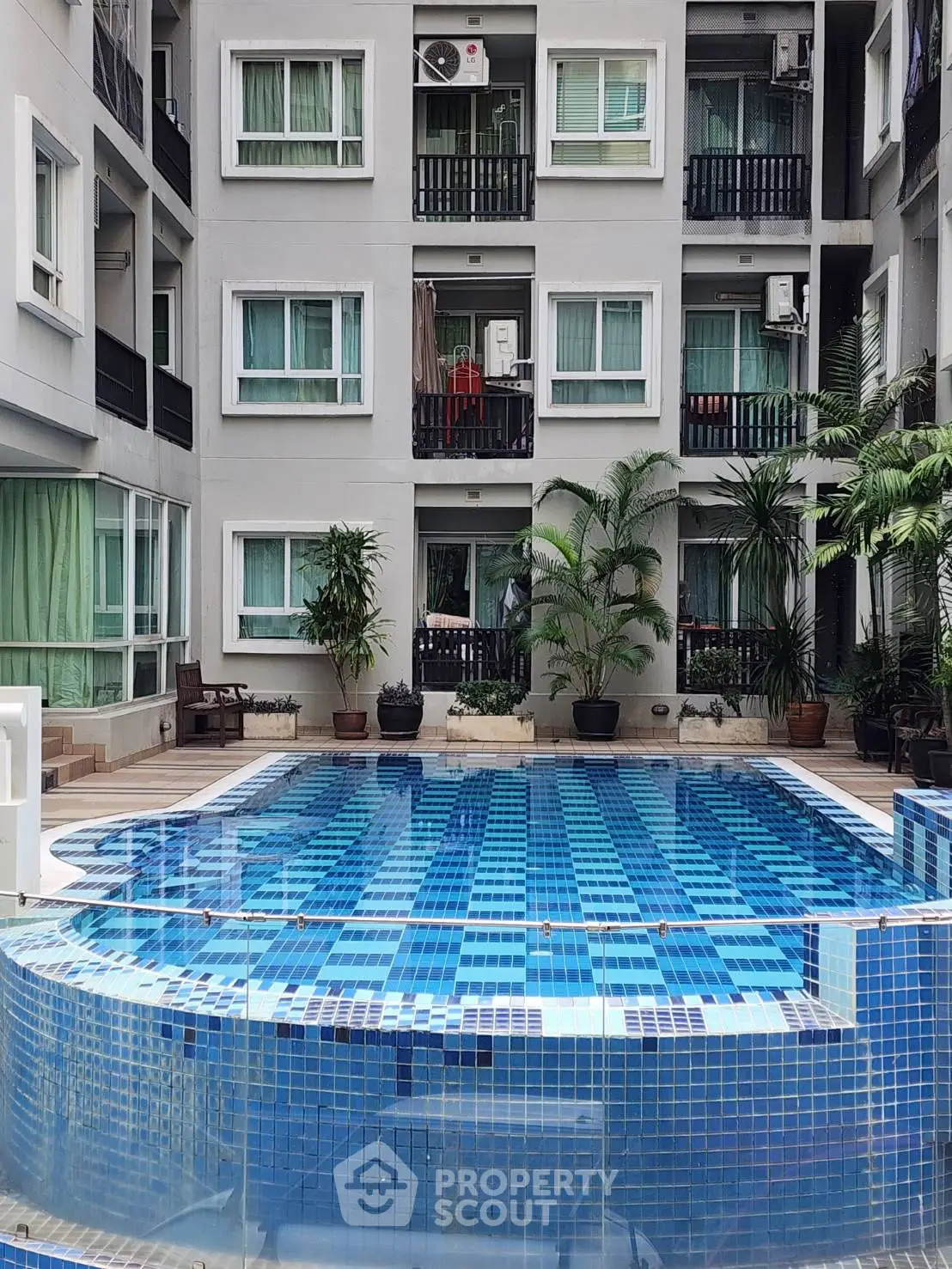 Luxurious apartment complex with a stunning blue-tiled swimming pool and lush greenery.