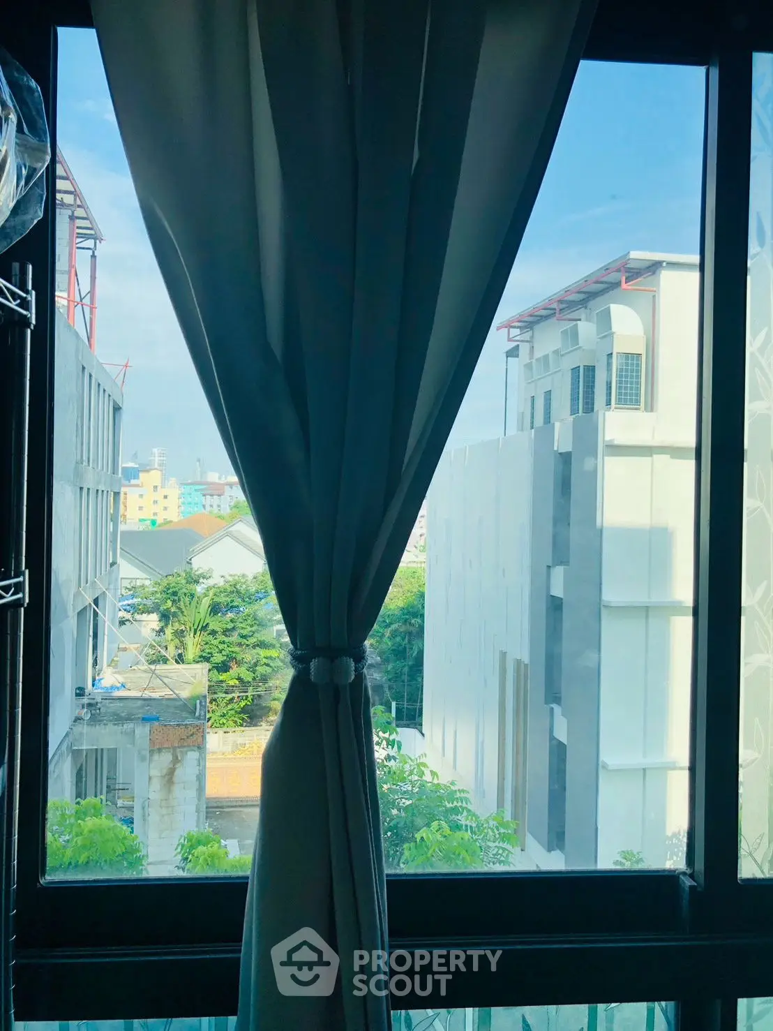 Bright urban view from window with modern buildings and lush greenery.