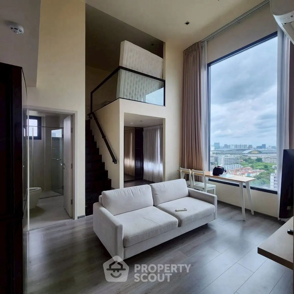 Spacious modern loft with large windows and city view, featuring a cozy living area and mezzanine bedroom.