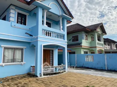 Charming two-story blue house with balcony and paved driveway in a serene neighborhood.