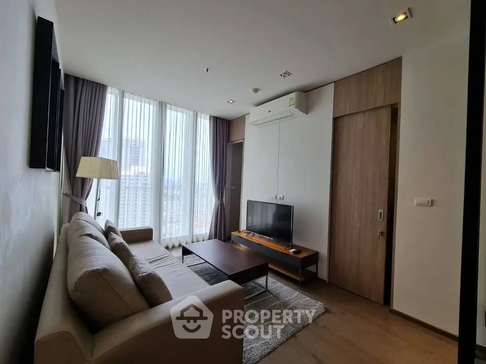 Modern living room with large windows and city view, featuring a cozy sofa and sleek TV setup.