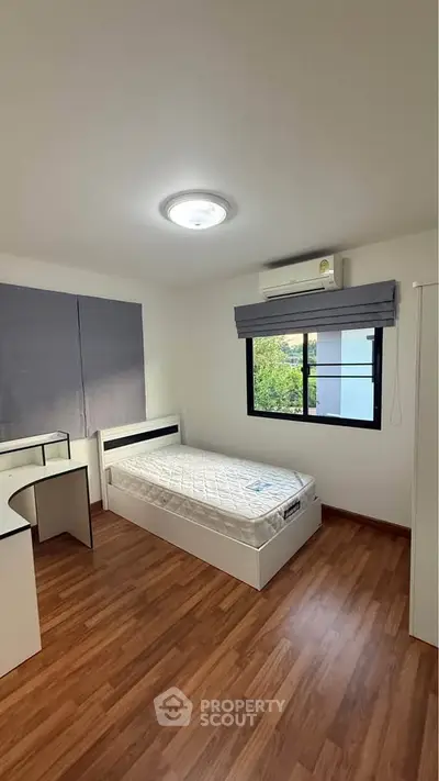 Modern bedroom with wooden flooring and natural light, featuring a single bed and desk.