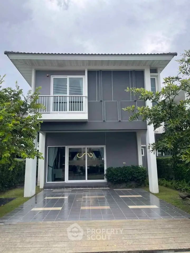 Modern two-story house with sleek design and spacious driveway, surrounded by lush greenery.