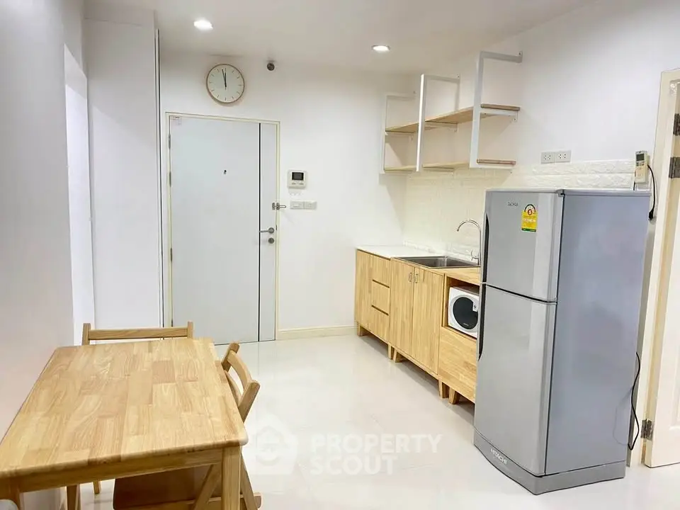 Modern kitchen with wooden cabinets, dining table, and stainless steel fridge in a cozy apartment.