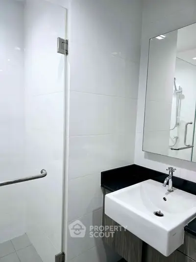 Modern bathroom with sleek sink and glass shower enclosure, featuring contemporary design and clean lines.