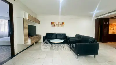Spacious living room with modern black leather sofas and wall-mounted TV, perfect for relaxation.