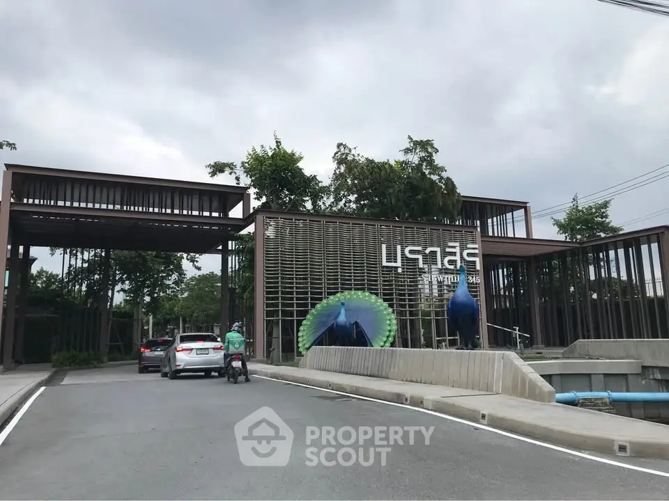 Modern gated entrance with unique architectural design and lush greenery.
