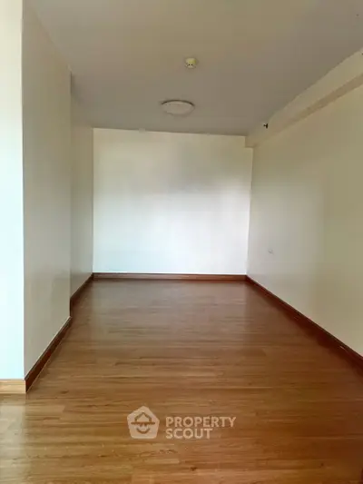 Spacious empty room with wooden flooring and white walls, ideal for customization.