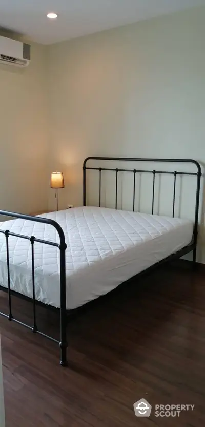 Cozy bedroom with minimalist metal bed frame and wooden flooring, perfect for a serene retreat.