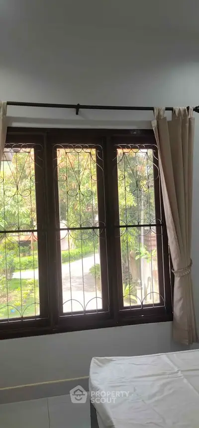 Bright bedroom with large window offering a serene garden view, perfect for relaxation.