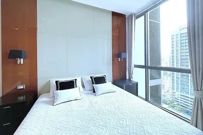 Luxurious bedroom with large windows offering stunning city views, modern decor, and elegant lighting.