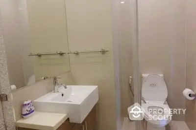 Modern bathroom with sleek fixtures, including a wall-mounted sink, toilet, and glass shower enclosure, accented by neutral tiles for a clean, minimalist aesthetic.