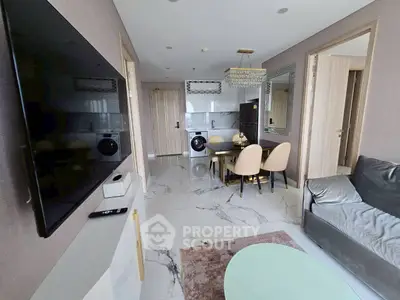 Modern living room with sleek furniture and open kitchen layout, featuring a wall-mounted TV and stylish dining area.