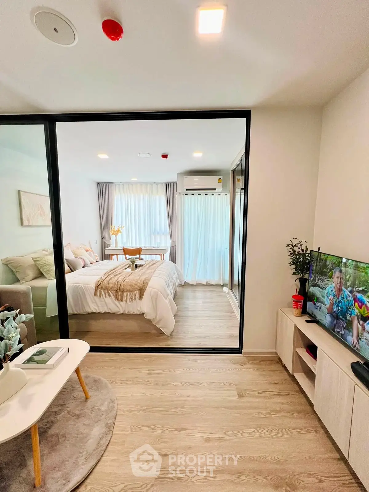 Modern open-plan living room with glass partition leading to a cozy bedroom, featuring stylish decor and natural light.