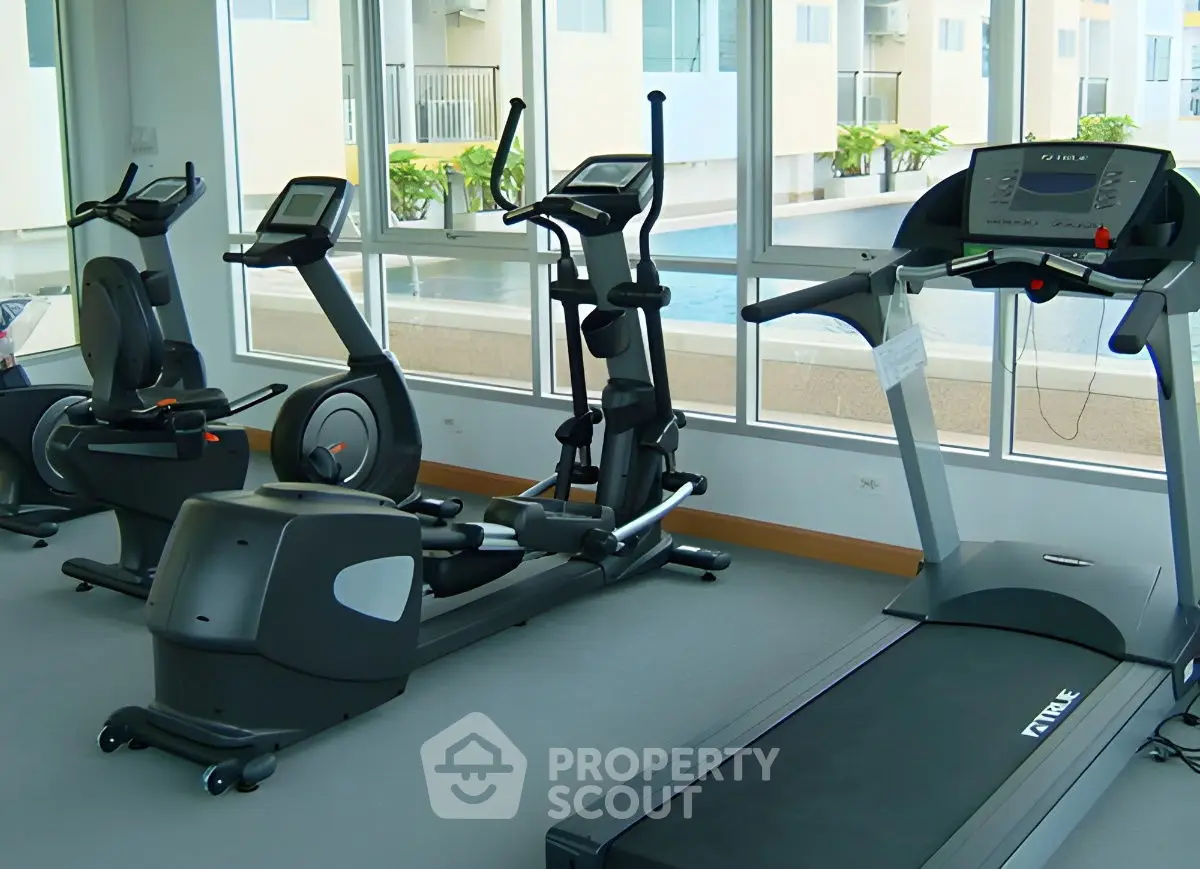 Modern gym with state-of-the-art equipment and pool view in luxury apartment complex.