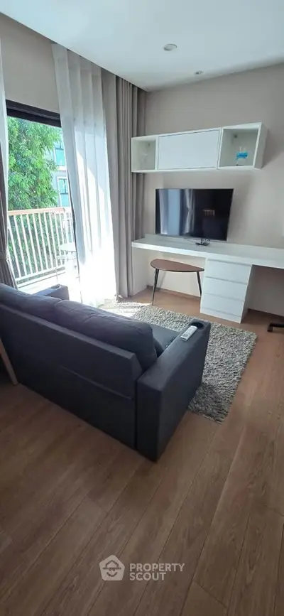 Modern living room with sleek furniture and large window offering natural light and balcony view.