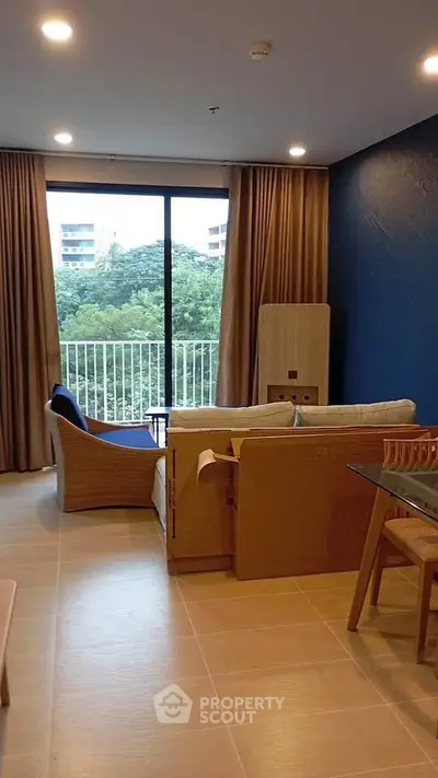 Modern living room with large windows and stylish furniture overlooking greenery.