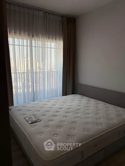 Cozy bedroom with large window and city view, featuring a comfortable mattress and elegant curtains.