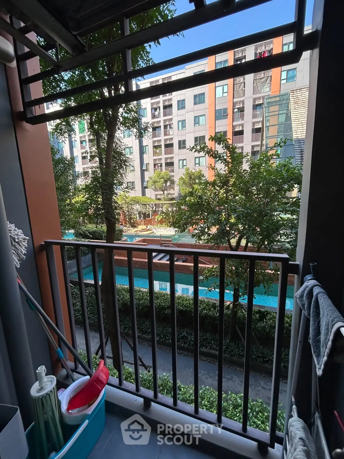 Charming balcony view overlooking a modern apartment complex with a pool and lush greenery.