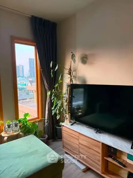 Cozy living room with large window and city view, featuring modern TV setup and lush indoor plants.