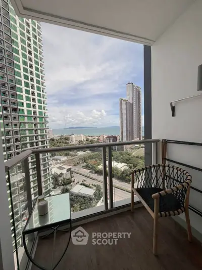 Modern balcony with stunning city and ocean view, featuring stylish chair and glass table.