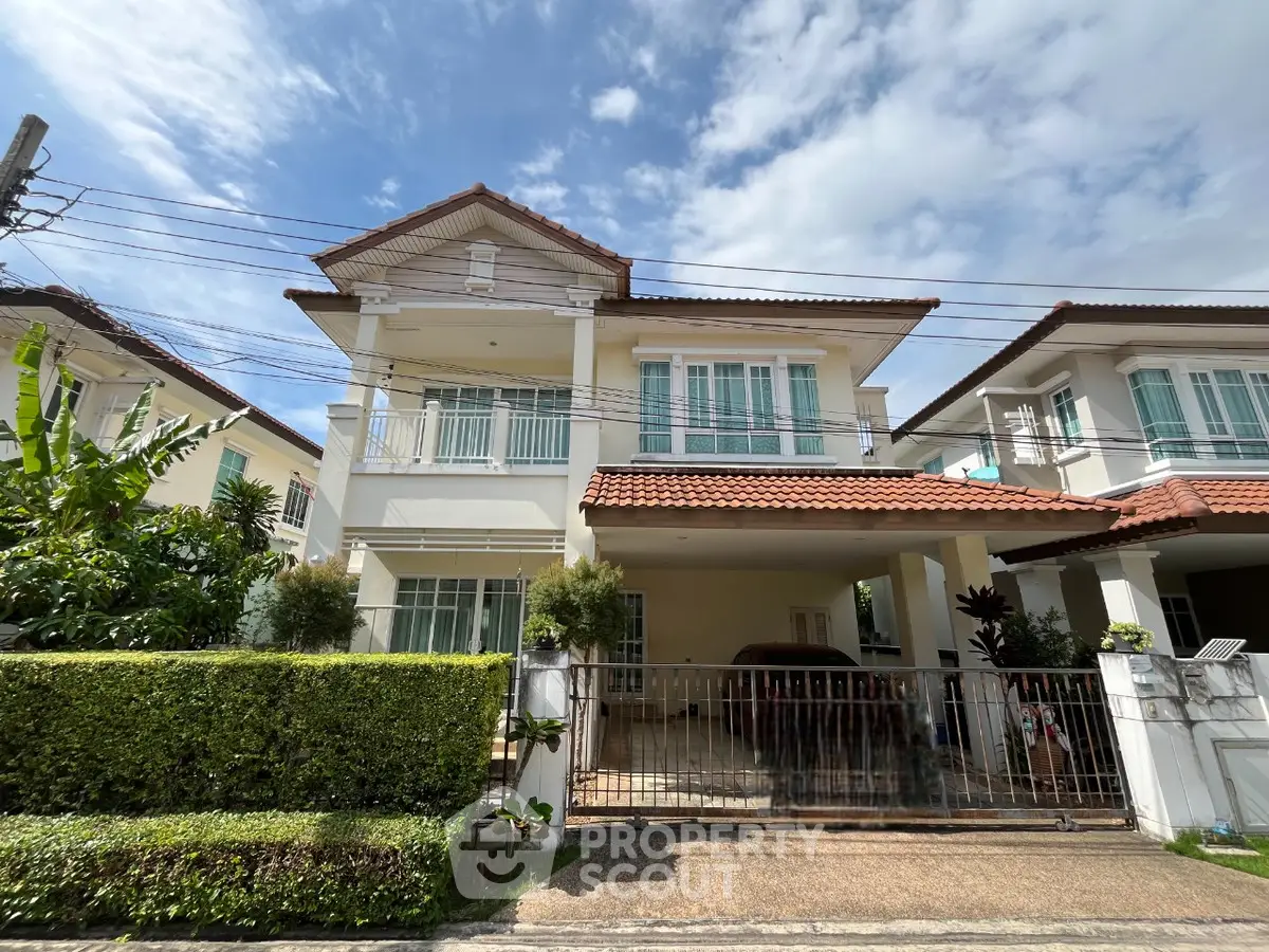 Charming two-story house with red-tiled roof and lush greenery in a serene neighborhood.