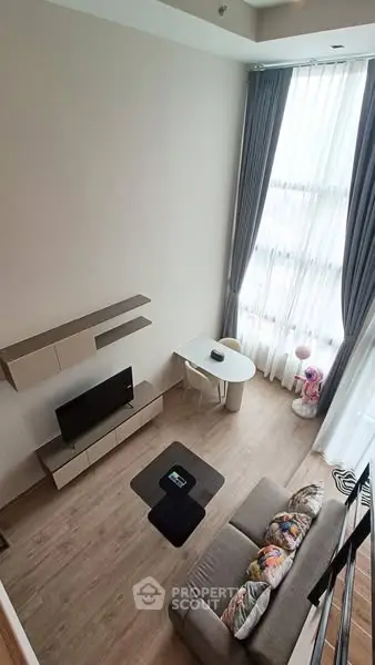 Modern living room with high ceiling and large window, featuring stylish furniture and elegant decor.