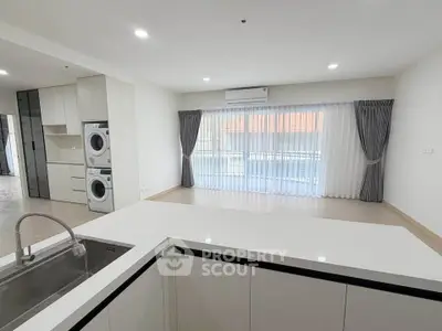 Spacious modern living room with open kitchen and laundry area, featuring large windows and elegant curtains.