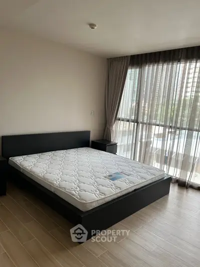 Spacious bedroom with large window and modern furnishings in urban apartment.