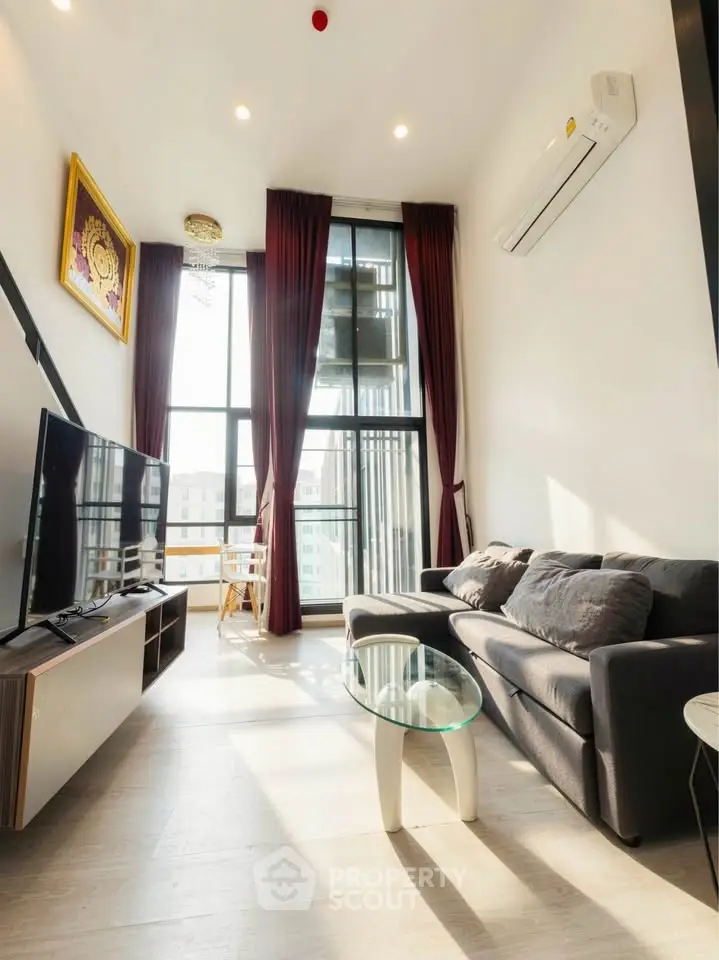 Modern living room with high ceilings, large windows, and stylish furniture in a bright apartment.