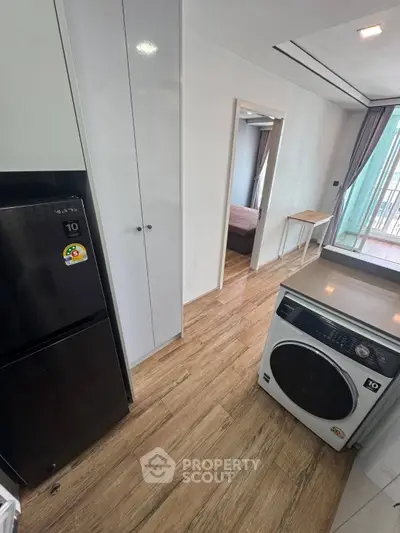 Modern apartment interior with sleek kitchen appliances and wooden flooring, leading to a cozy bedroom.