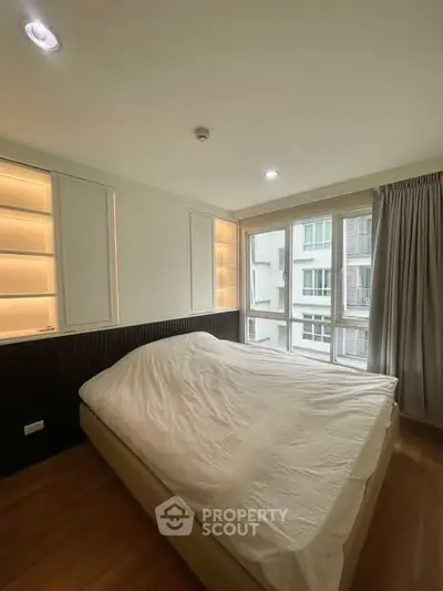 Modern bedroom with large windows and built-in shelving, offering ample natural light.