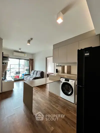 Modern open-plan living room with kitchen featuring washing machine and balcony view.
