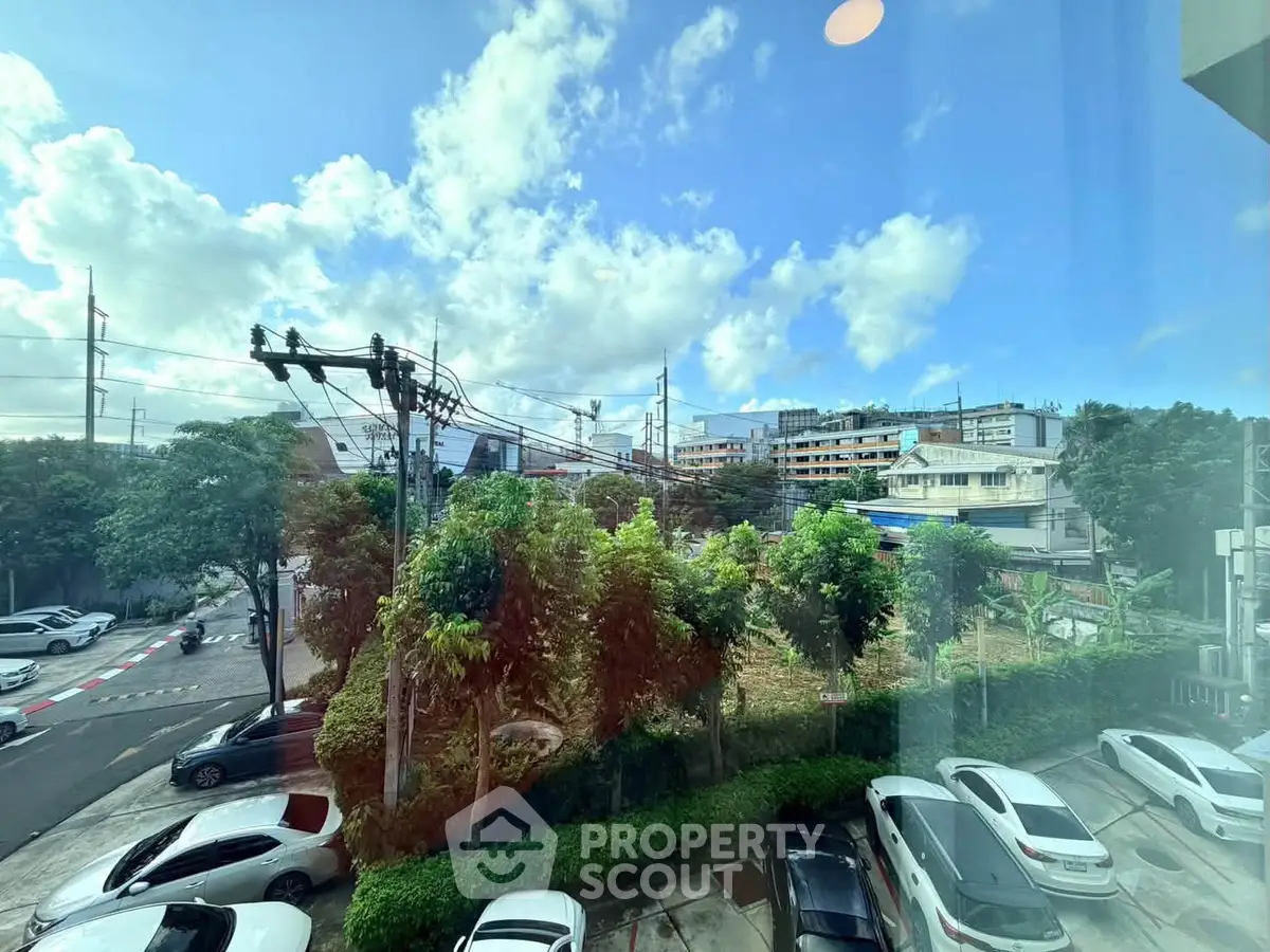 Scenic urban view from a window showcasing lush greenery and parked cars under a bright blue sky.