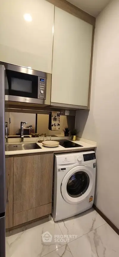 Modern compact kitchen with washing machine and microwave, sleek cabinetry, and marble flooring.
