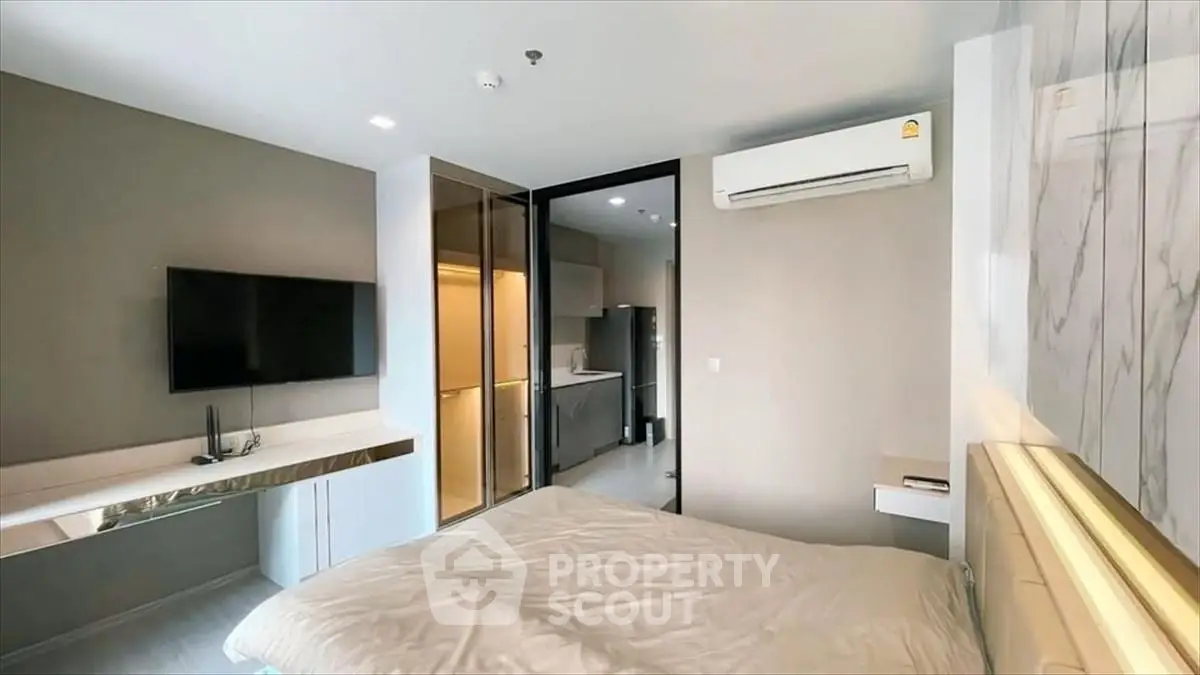 Modern bedroom with sleek design, featuring a wall-mounted TV and air conditioning, adjacent to a stylish kitchen.