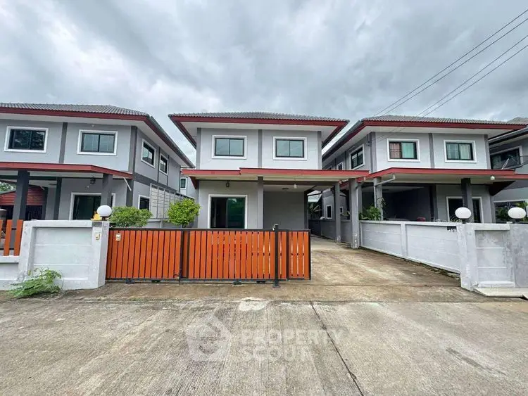 Modern two-story homes with gated entrance and driveway under cloudy sky.