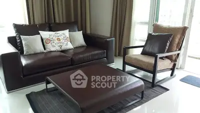 Modern living room with sleek leather sofa and armchair, featuring elegant decor and natural light.