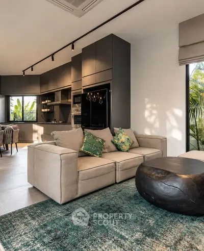 Modern living room with stylish furniture and open kitchen layout, featuring lush greenery outside.