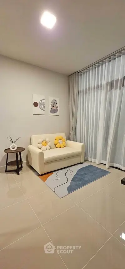 Cozy living room with modern decor and large window draped with sheer curtains.