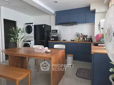 Modern kitchen with blue cabinets, wooden dining table, and stacked washer-dryer in a stylish open layout.