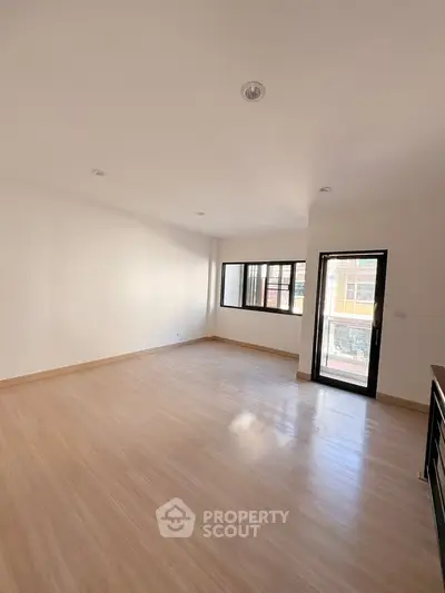 Spacious empty room with wooden flooring and large windows for natural light.