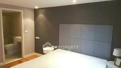 Modern bedroom with ensuite bathroom, featuring a stylish headboard and wooden flooring.