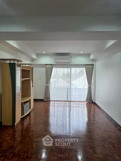 Spacious living room with polished wooden floors and large window for natural light.