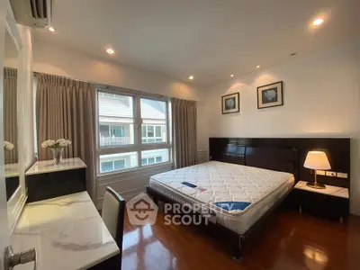Spacious bedroom with large window and elegant furnishings in modern apartment.