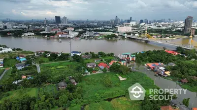 Aerial view of riverside properties with lush greenery and city skyline in the background.