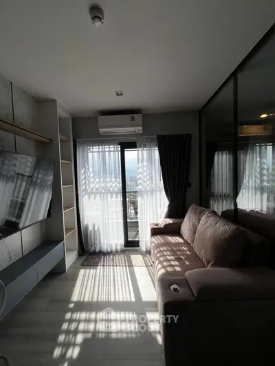 Modern living room with large window and balcony view, featuring a sleek sofa and wall-mounted TV.